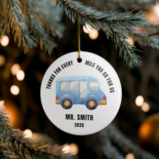 Round Christmas ornament with a blue bus and text, hanging on a tree.