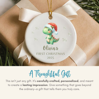 Christmas ornament with a dinosaur design and text 'Olivia's First Christmas 2025' on a gift box.