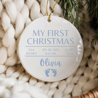 Round white ornament with blue text and baby details on a textured beige surface.